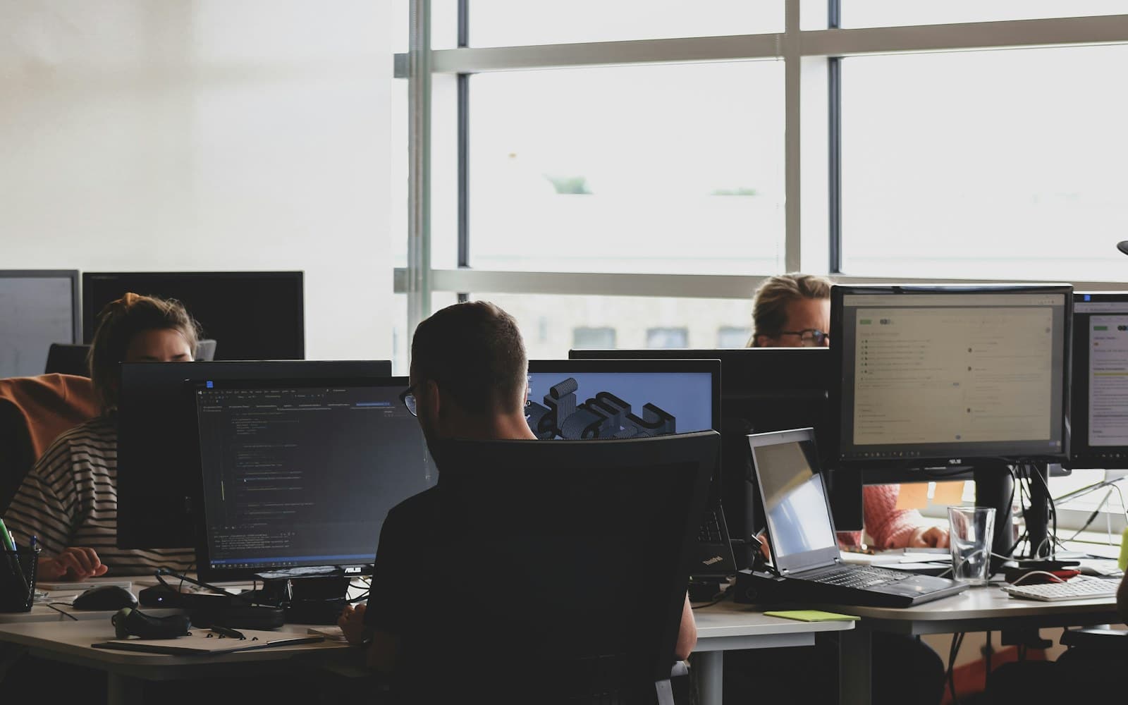 Three developers working at adjacent desktop monitors