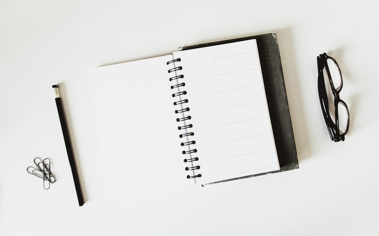 An open blank notebook beside reading glasses on a white desk